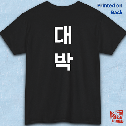 black t-shirt backside flatlay with “대박” Daebak Korean slang Hangeul text printed in white by K-Jota