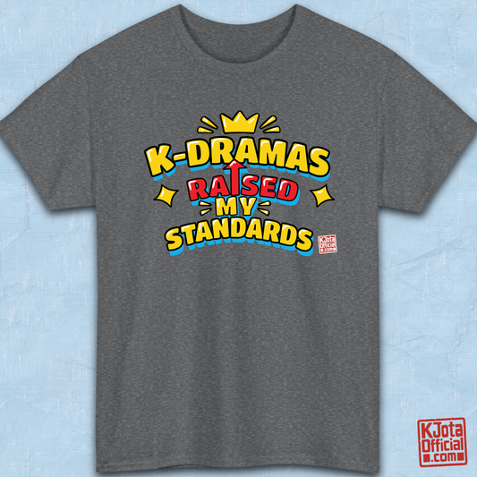 'K-DRAMAS RAISED MY STANDARDS' yellow, red, and blue lettering with an uparrow in place of letter “I” printed on a gray t-shirt flatlay. Realistic expectations K-fan graphic t-shirt by K-Jota