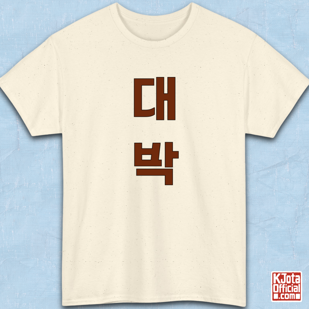 beige t-shirt flatlay with “대박” Daebak Korean slang Hangeul text printed in burgundy brown by K-Jota