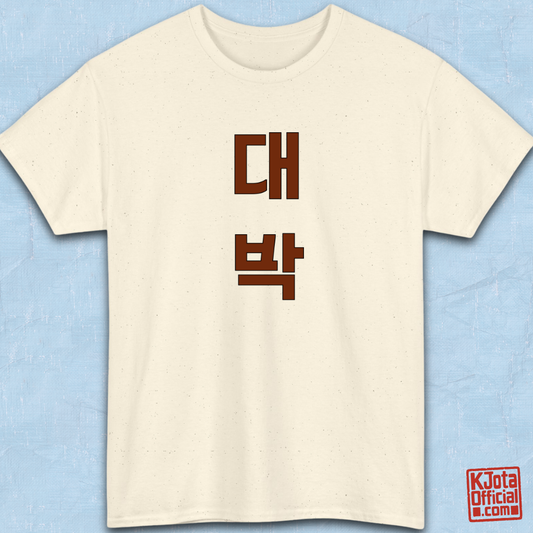 beige t-shirt flatlay with “대박” Daebak Korean slang Hangeul text printed in burgundy brown by K-Jota