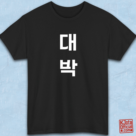 black t-shirt flatlay with “대박” Daebak Korean slang Hangeul text printed in white by K-Jota