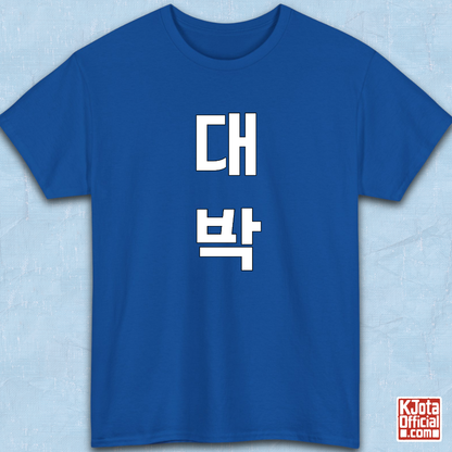 blue t-shirt flatlay with “대박” Daebak Korean slang Hangeul text printed in white by K-Jota