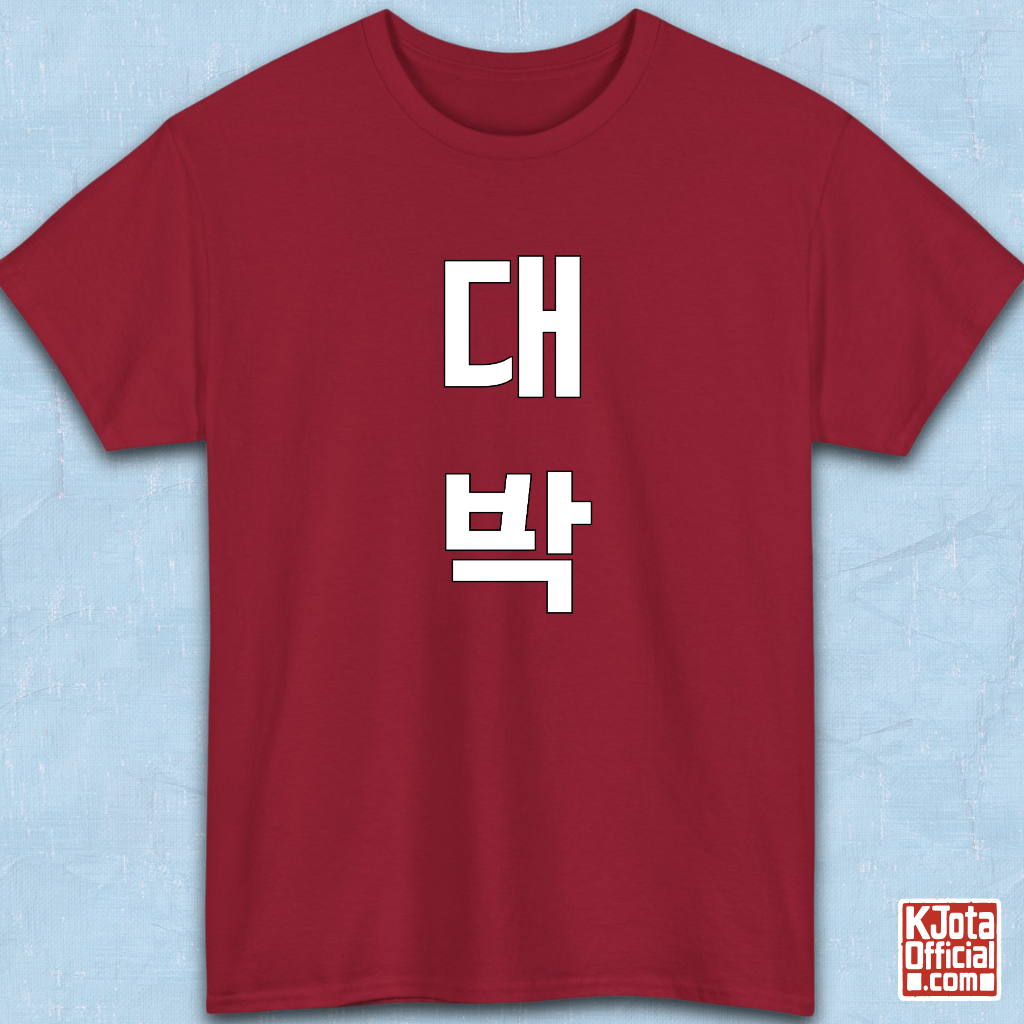 red t-shirt flatlay with “대박” Daebak Korean slang Hangeul text printed in white by K-Jota