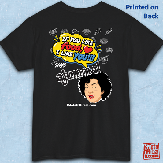 black t-shirt backside flatlay with a comic-style yellow speech bubble reading 'If You Like Food, I Like You!!!' above a laughing Korean ajumma illustration and hand-drawn Korean food icons by K-Jota