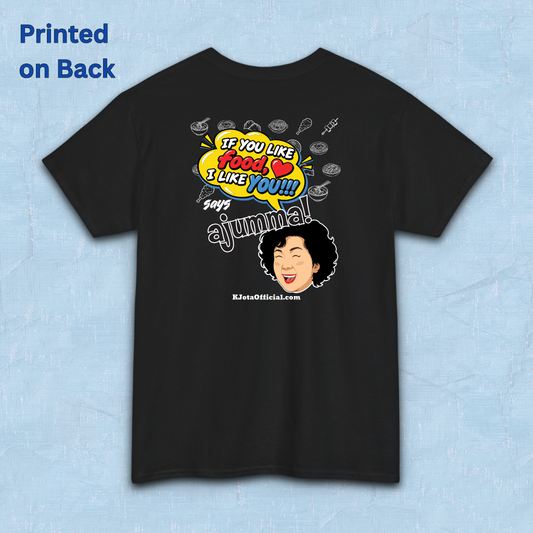 black t-shirt backside flatlay with a comic-style yellow speech bubble reading 'If You Like Food, I Like You!!!' above a laughing Korean ajumma illustration and hand-drawn Korean food icons by K-Jota