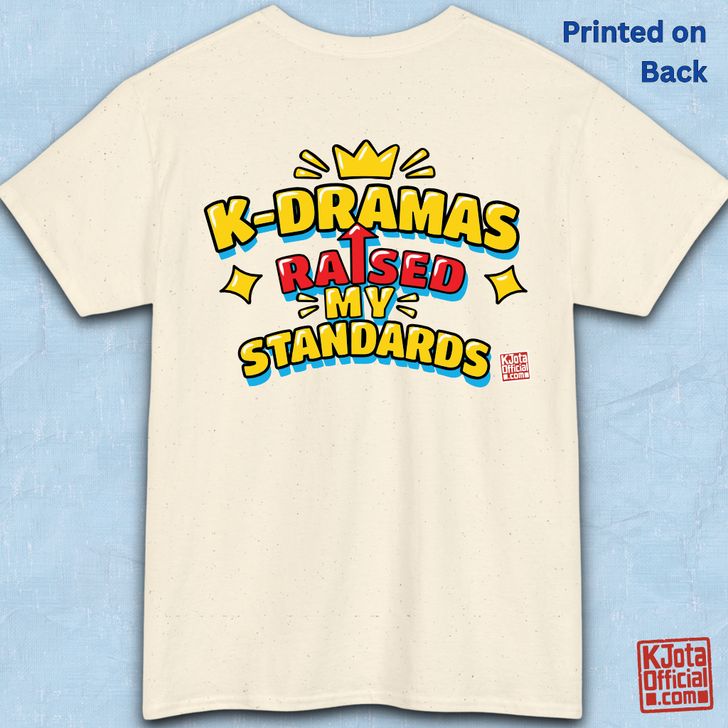'K-DRAMAS RAISED MY STANDARDS' yellow, red, and blue lettering with an uparrow in place of letter “I” printed on a beige t-shirt backside flatlay. Realistic expectations K-fan graphic t-shirt by K-Jota