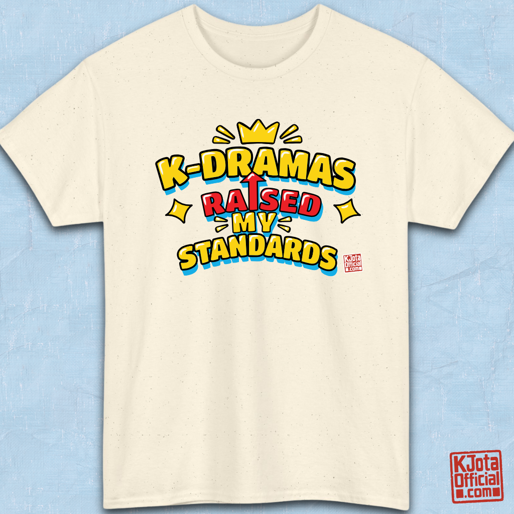 'K-DRAMAS RAISED MY STANDARDS' yellow, red, and blue lettering with an uparrow in place of letter “I” printed on a beige t-shirt flatlay. Realistic expectations K-fan graphic t-shirt by K-Jota