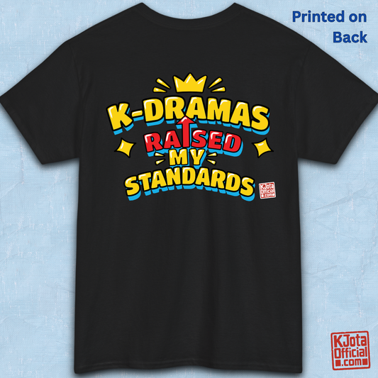 'K-DRAMAS RAISED MY STANDARDS' yellow, red, and blue lettering with an uparrow in place of letter “I” printed on a black t-shirt backside flatlay. Realistic expectations K-fan graphic t-shirt by K-Jota