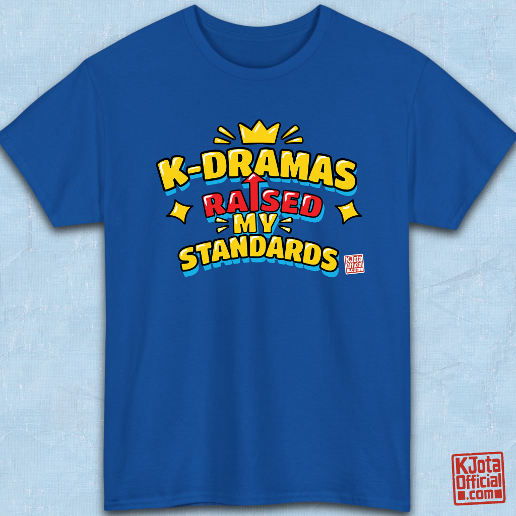 K-DRAMAS RAISED MY STANDARDS' yellow, red, and blue lettering with an uparrow in place of letter “I” printed on a blue t-shirt flatlay. Realistic expectations K-fan graphic t-shirt by K-Jota