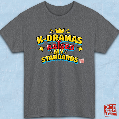 'K-DRAMAS RAISED MY STANDARDS' yellow, red, and blue lettering with an uparrow in place of letter “I” printed on a gray t-shirt flatlay. Realistic expectations K-fan graphic t-shirt by K-Jota