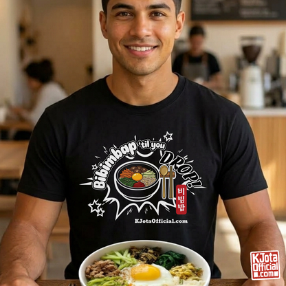 A man wearing a black t-shirt by K-Jota showing Korean food mixed rice bowl and sitting at a table with a bowl of bibimbap. The graphic features a hand-illustrated bowl of bibimbap with a spoon and chopsticks, and texts “Bibimbap ‘til You Drop 비빔밥” and “KJotaOfficial.com”.