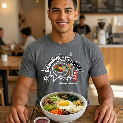 A man wearing a gray t-shirt by K-Jota showing Korean food mixed rice bowl and sitting at a table with a bowl of bibimbap. The graphic features a hand-illustrated bowl of bibimbap with a spoon and chopsticks, and texts “Bibimbap ‘til You Drop 비빔밥” and “KJotaOfficial.com”.