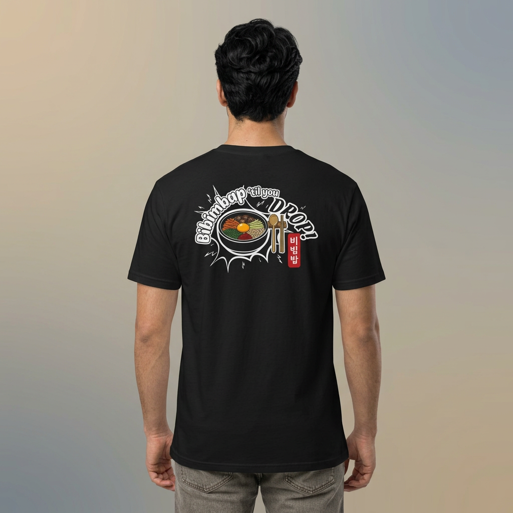 A man viewed from behind wearing a black Korean food fan t-shirt by Kjota with a graphic on the back. The graphic features a bowl of bibimbap with a spoon and chopsticks, and text “Bibimbap ‘til You Drop 비빔밥”