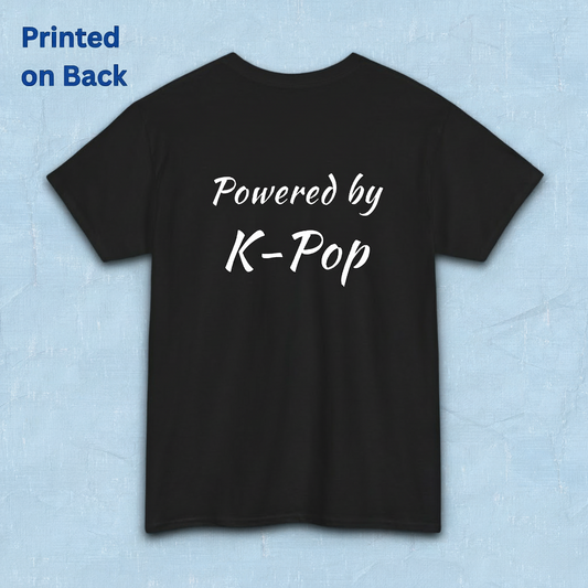 A black short-sleeve t-shirt flatlay with 'Powered by K-Pop' printed in white script on the back, displayed against a light blue textured background by Kjota