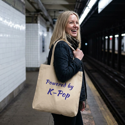 woman holding a Powered by K-pop beige canvas tote bag for photocard trading events by Kjota