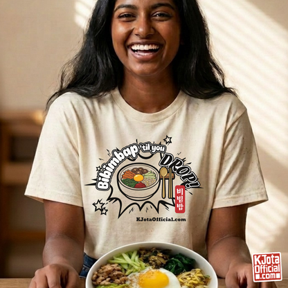 A woman wearing a beige t-shirt by K-Jota showing Korean food mixed rice bowl and sitting at a table with a bowl of bibimbap. The graphic features a hand-illustrated bowl of bibimbap with a spoon and chopsticks, and texts “Bibimbap ‘til You Drop 비빔밥” and “KJotaOfficial.com”.
