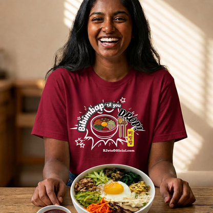 A woman wearing a red t-shirt by K-Jota showing Korean food mixed rice bowl and sitting at a table with a bowl of bibimbap. The graphic features a hand-illustrated bowl of bibimbap with a spoon and chopsticks, and texts “Bibimbap ‘til You Drop 비빔밥” and “KJotaOfficial.com”.