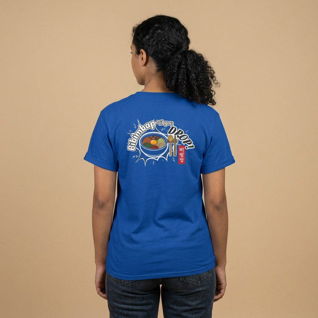 A woman viewed from behind wearing a blue Korean food fan t-shirt by Kjota with a graphic on the back. The graphic features a bowl of bibimbap with a spoon and chopsticks, and text “Bibimbap ‘til You Drop 비빔밥”