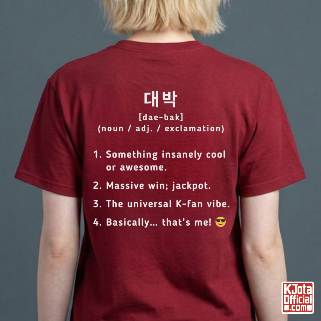 woman wearing a red short-sleeve T-shirt shown from the back with white printed Korean text and a dictionary-style definition of Daebak 대박 Korean slang. K-fandom merch by K-Jota