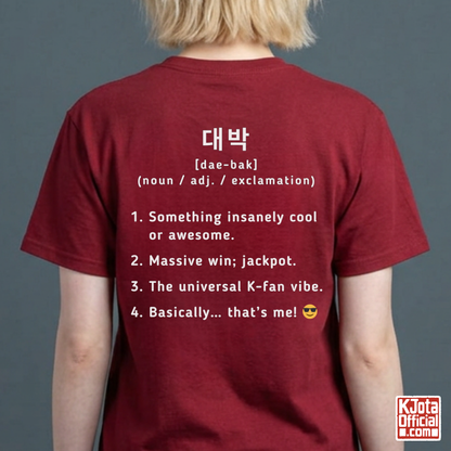 woman wearing a red short-sleeve T-shirt shown from the back with white printed Korean text and a dictionary-style definition of Daebak 대박 Korean slang. K-fandom merch by K-Jota